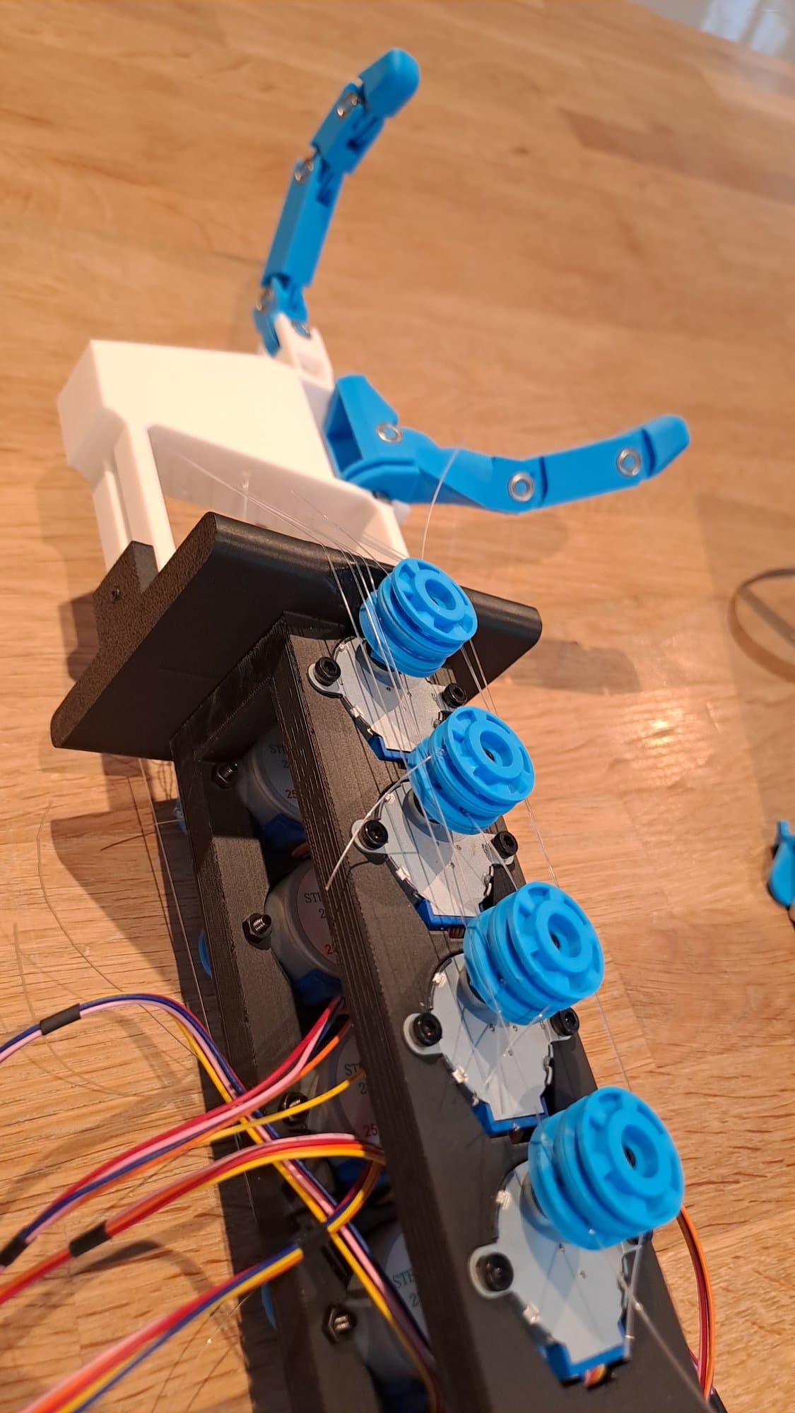 The forearm column with stepper motors and blue tendon spools, with the fingers on top.